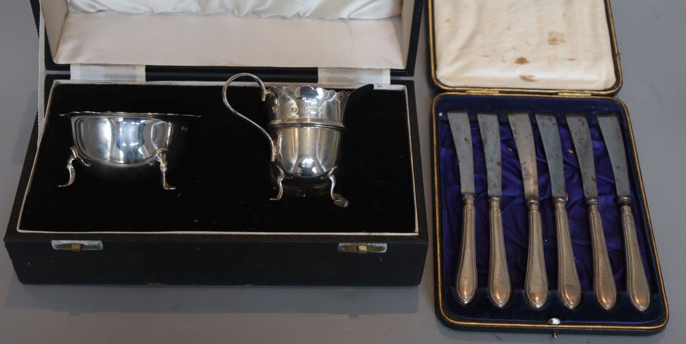 A cased matched silver cream jug and sugar bowl, 1915 & 1931 and a cased set of six knives.